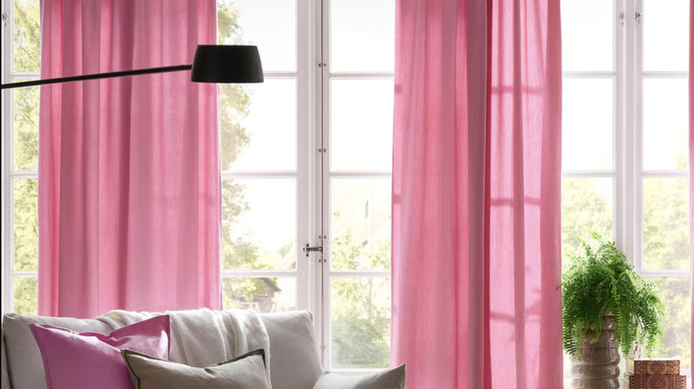 IKEA's GINSTMOTT curtains in bright pink hang in a living room with a flor lamp and chair