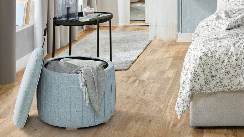 Open blanket-filled  ÅTERLÖGA storage pouffe in bedroom