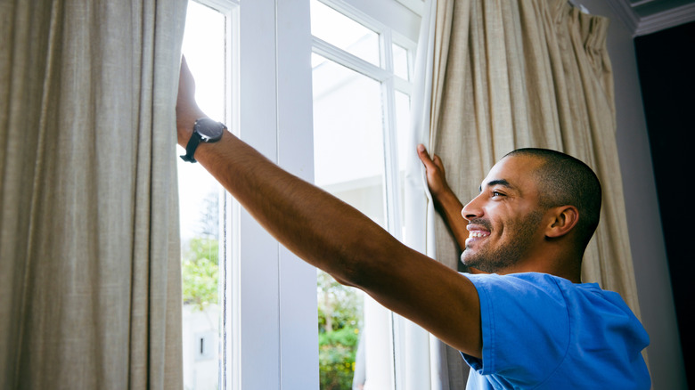Man opening curtains wide