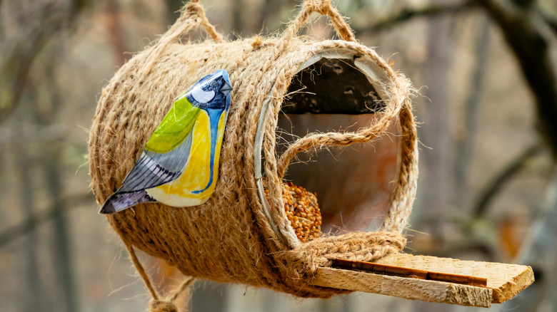 can birdhouse with rope around it and a perch and fake bird attached