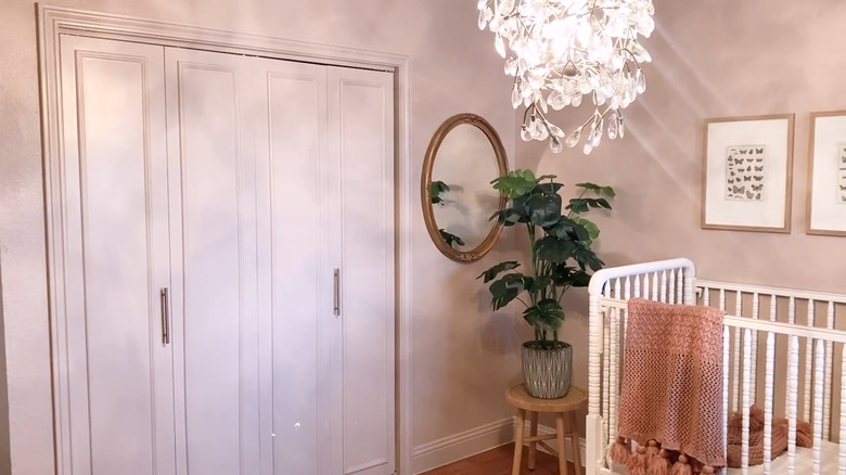 pink bifold closet doors with trim and chrome hardware with a plant and mirror beside it
