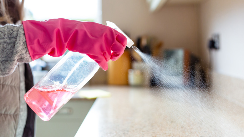A hand with a pink rubber glove spraying cleaning solution on a countertop.