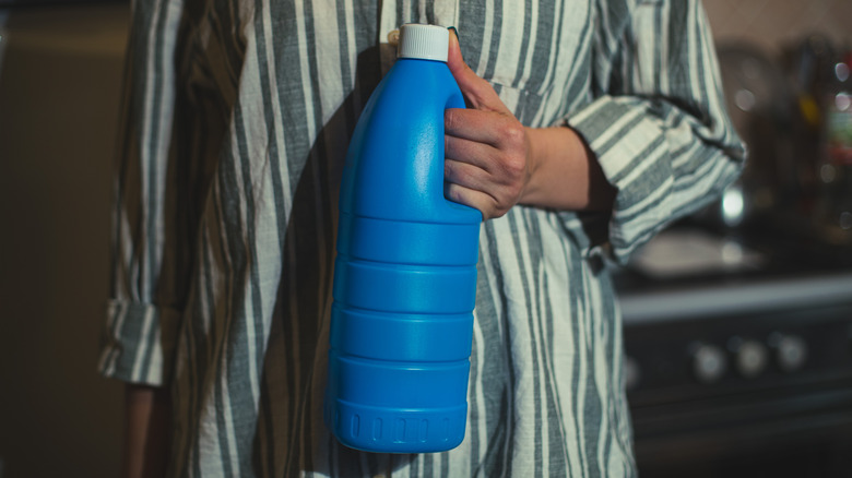 A person holding a bottle of bleach.