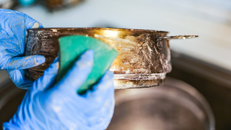 Person wearing blue rubber gloves to sponge clean a rusty pot.