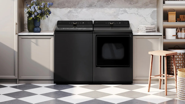 Black LG washer and dryer in a modern laundry room with beige cabinest and a marble backsplash