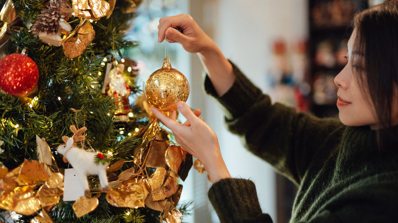 A woman hanging a gold Christmas ornament