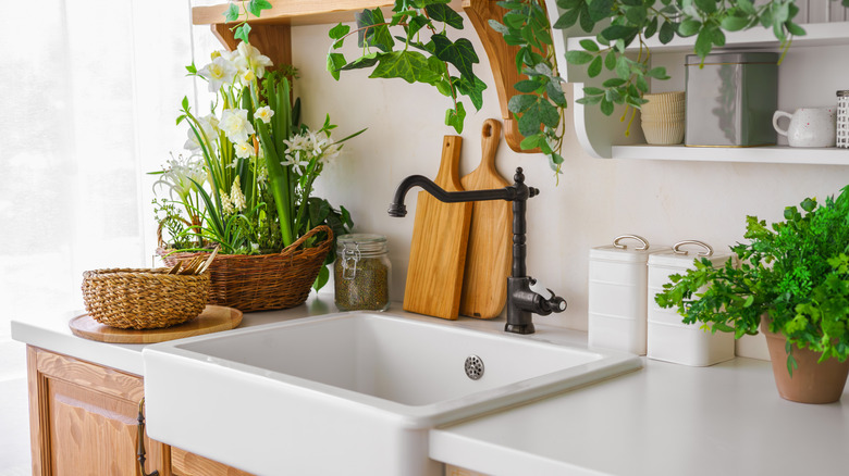 A white sink surrounded by fresh flowers, herbs, and food preparation boards
