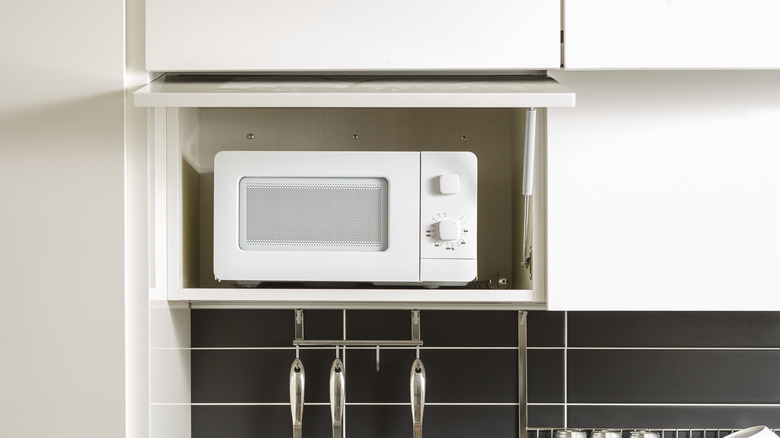 An open cupboard revealing a microwave stored inside