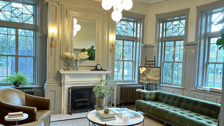 A foyer with green couch, marble coffee table, and windows with trim that matches the wall panels