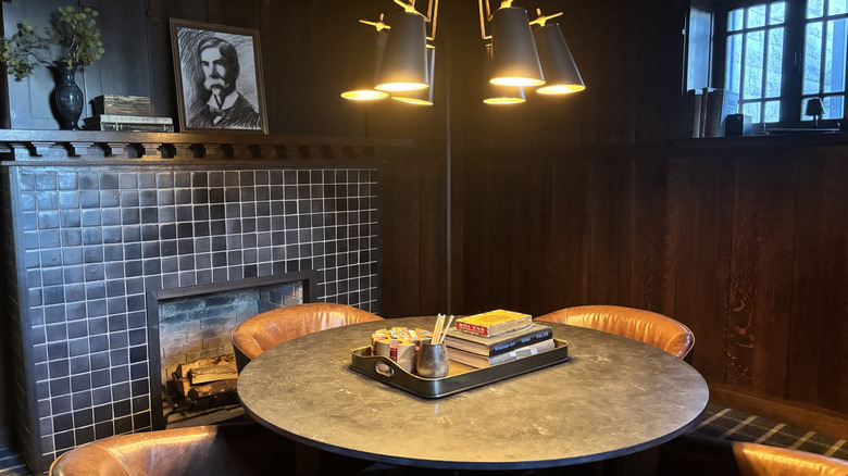 A dark room with a stone table, black tiled fireplace, and dark wood wall paneling