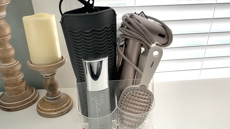 Hair styling tools and products tucked into kitchen cutlery organizer beside candles and window