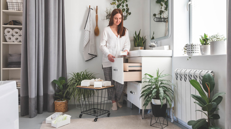 Happy young woman organizing white bathroom filled with plants
