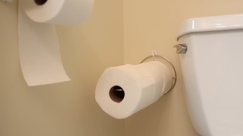 A paper towel holder being used beside the toilet for extra storage