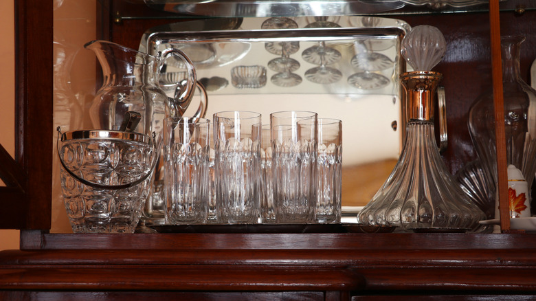 A glass-front vintage bar cabinet with glasses and decanters.