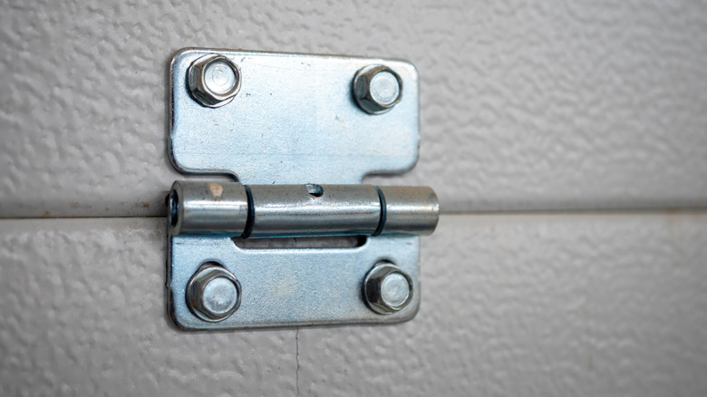 Close-up of a hinge on a white, textured garage door
