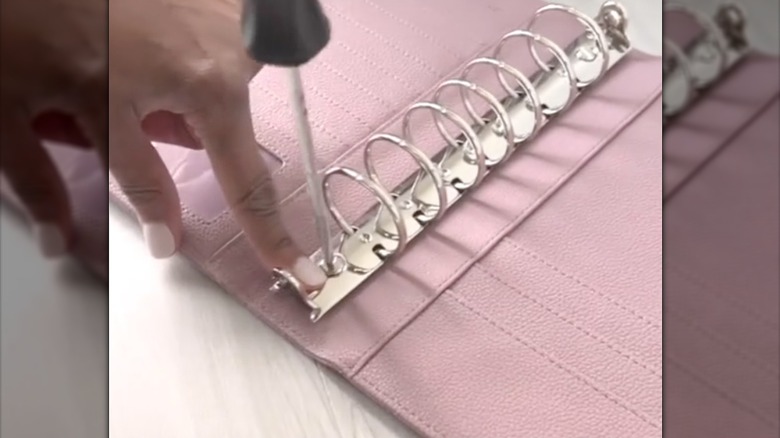 someone screwing in a metal binder spine into a pink leather folder