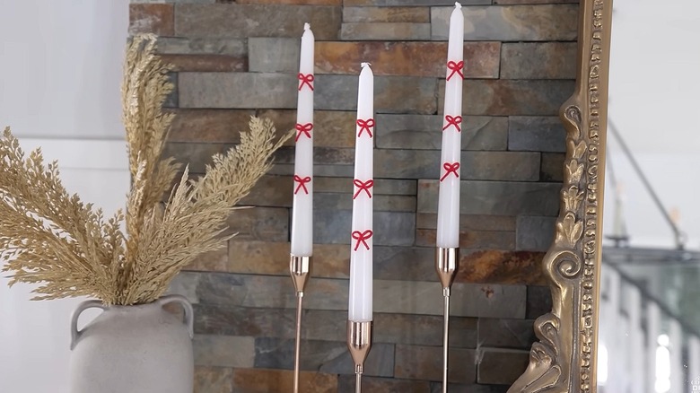 Three taper candles decorated with red wax bows in metallic taper holders