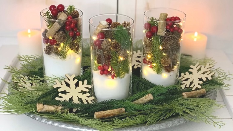 Centerpiece made with a Dollar Tree charger and three glass vases filled with holiday items and surrounded by pine boughs and accents