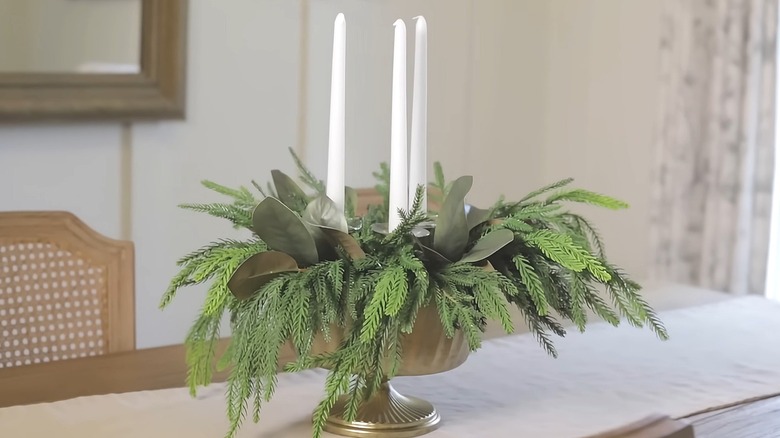 Elegant centerpiece in an elevated bowl with taper candles and greenery sitting on a dining table