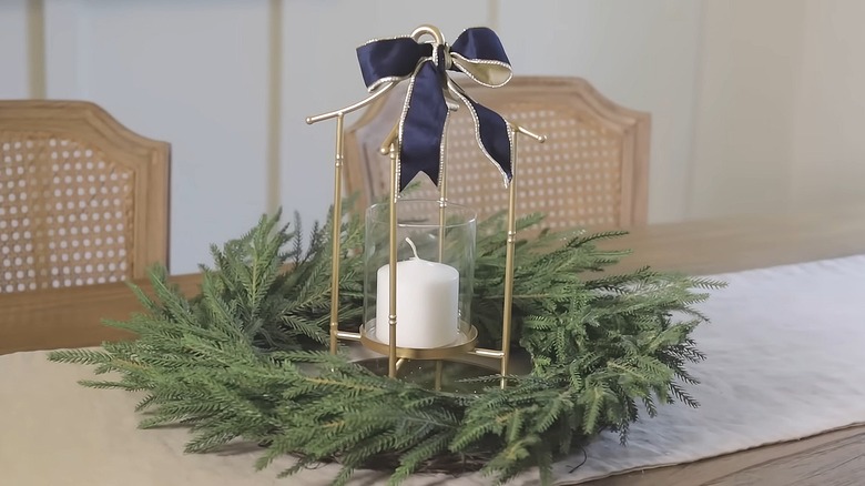 Artificial evergreen wreath with a lantern in the middle sitting on a table runner