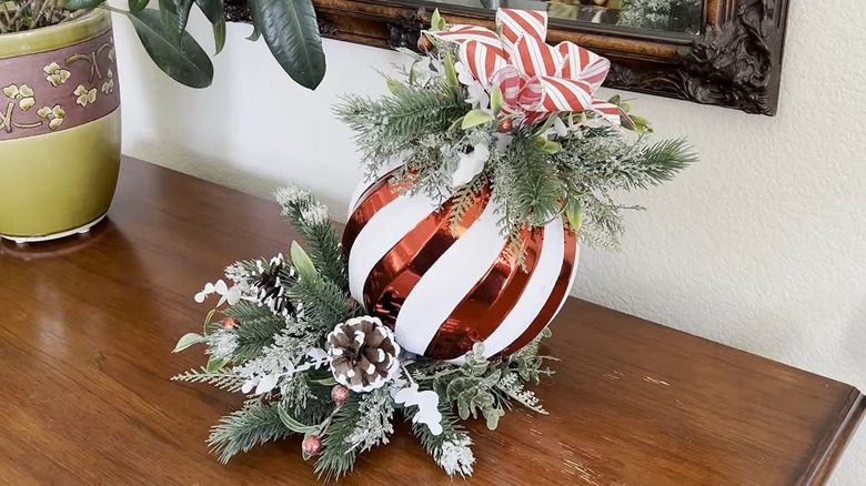 Giant ornament surrounded by pine boughs with a bow on top