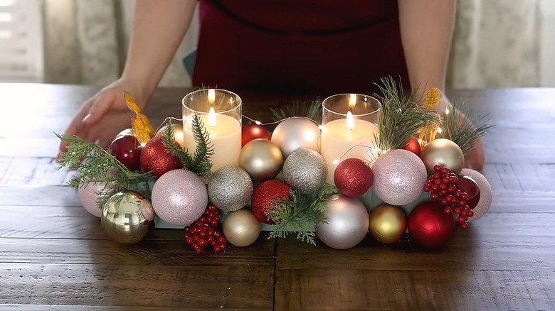 Woman positioning a centerpiece with ornaments, greenery, candles, and fairy lights