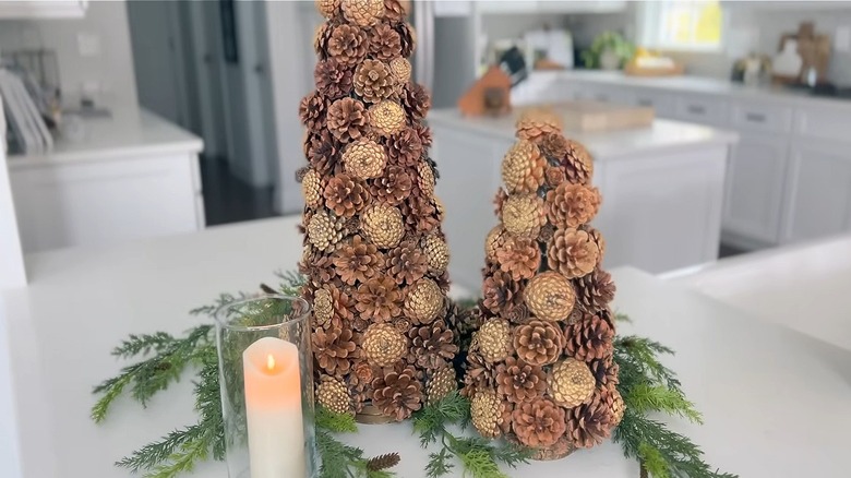 Two pine cone covered trees with greenery around them and a candle next to them