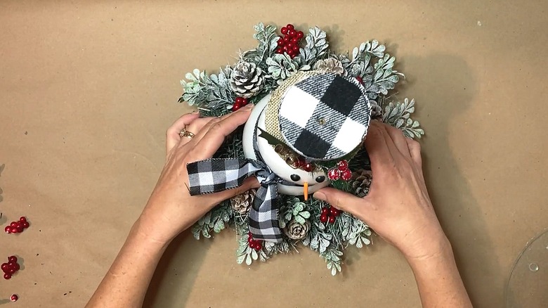 Person placing the snowman in the middle of a wreath