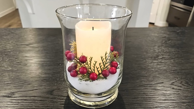 Wide glass vase with artificial snow in the bottom and berries on top with a candle in the middle