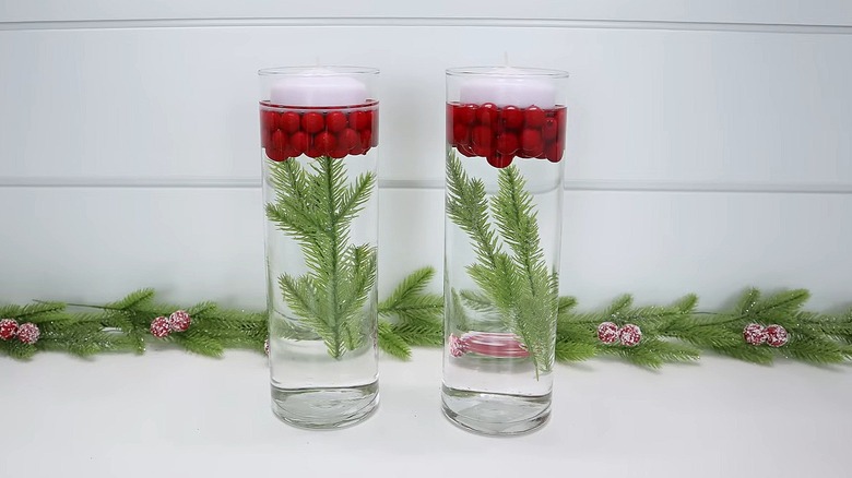 Clear glass cylinder vases filled with water and artificial pine boughs, berries, and floating candles