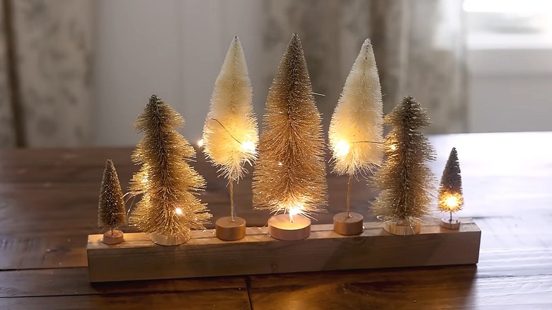 Wood board with bottle brushes glued to it and fairy lights woven among the trees