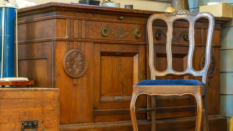 Vintage wooden sideboard with carved details and brass handles, accompanied by a wooden upholstered chair