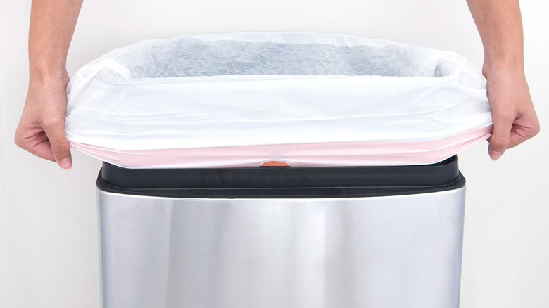 Person pulling sturdy 13 gallon kitchen bag over stainless steel trash can