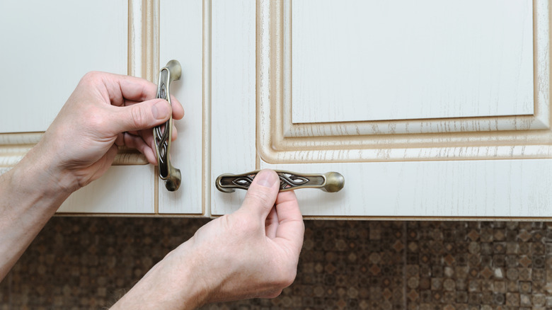 putting original hardware back on kitchen cabinets that has been cleaned to remove paint