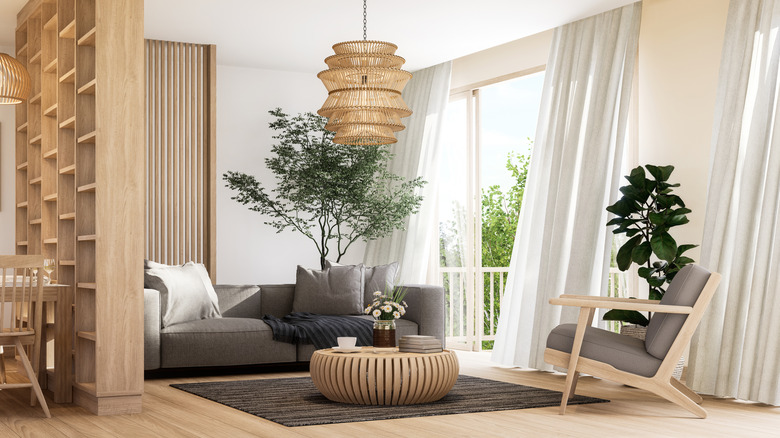 Contemporary living room with gray sofa, wooden accents, and white curtains blowing in the wind divided from dining by a wooden built-in partition