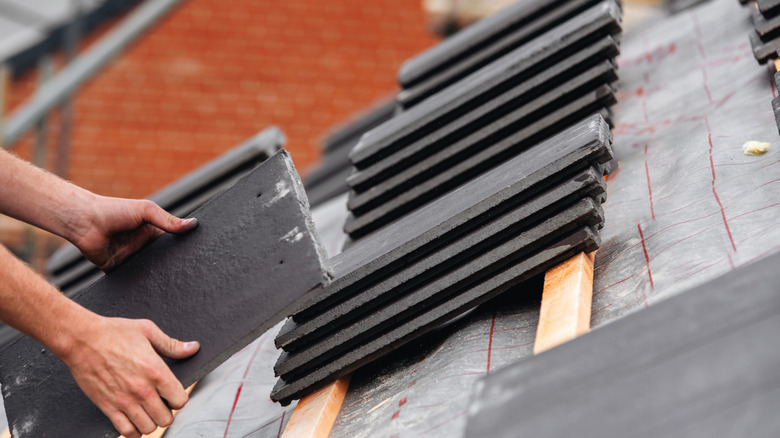 Close-up of roofing contractor's hands placing slate tiles on roof