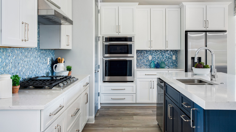 White kitchen with darke blue island and light blue backsplash with natural light