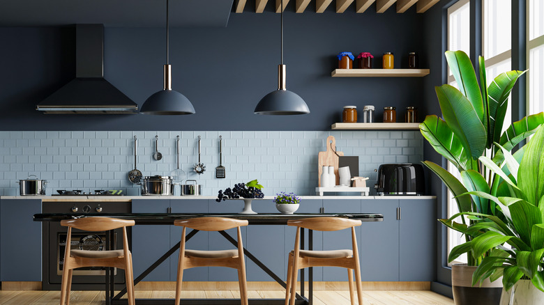 Open kitchen with large window, table, and deep blue walls and cabinets with light blue backsplash