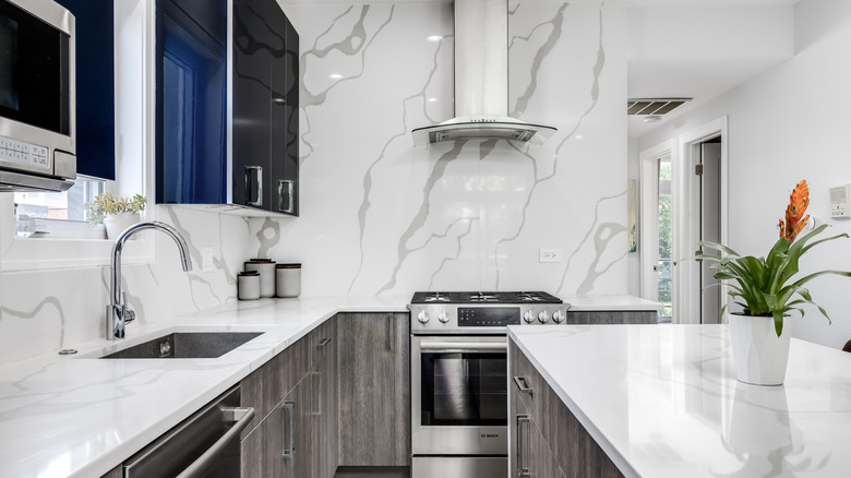 Modern kitchen with dark blue upper cabinets and grey wood lower cabinets and marble walls