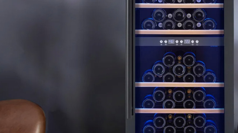 The Wine Enthusiast Vinotech Dual Zone Wine Cellar with bottles and next to a cabinet and chair