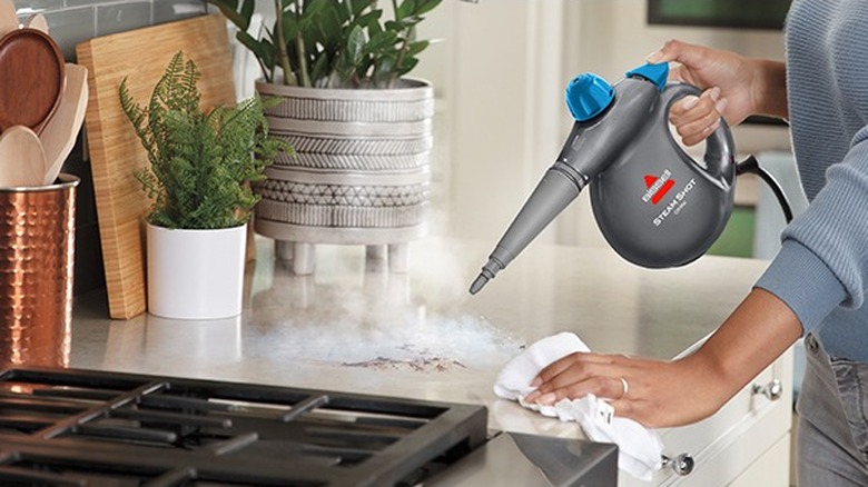 Female hands using a portable steam cleaner on a kitchen countertop