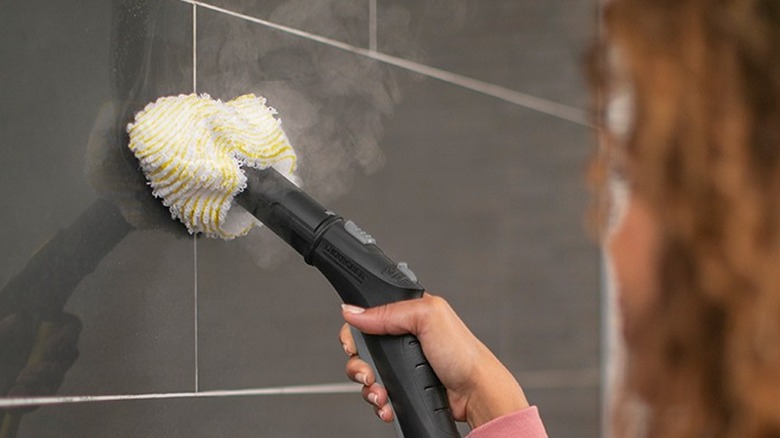 Woman using a steam cleaner on shower tile grout