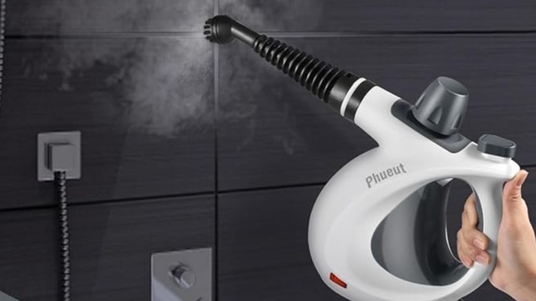 Hand holding a steam cleaner close to a tile's grout