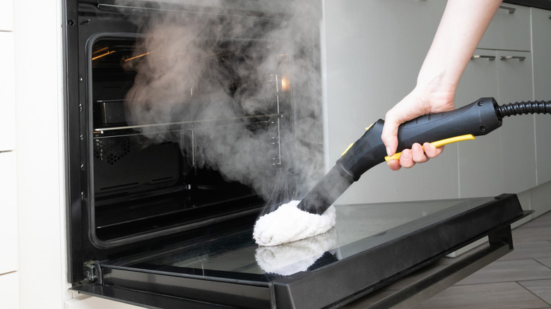 Hand using a steam cleaner to wipe an oven's door