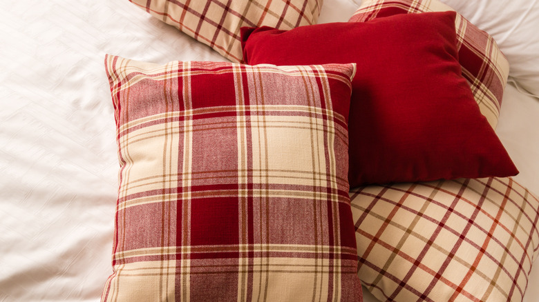 Fall plaid, tartan, and solid pillows in red and cream on an off-white blanket.