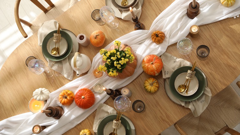 A bunched up, white table runner decorated with vintage butter churners and pumpkins