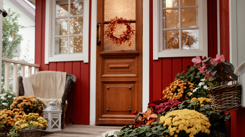 A wooden and frosted glass door with a simple autumn wreath with wicker chairs and flowers in wicker baskets on the front porch