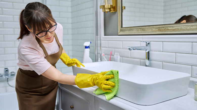 Woman using spray cleaner on the side of a sink