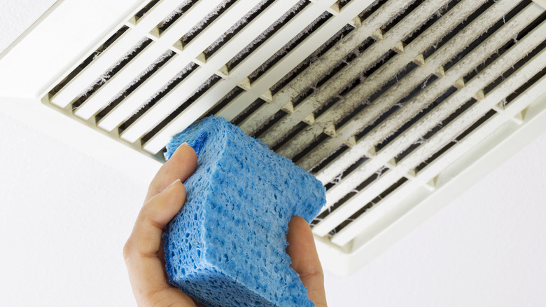 Dusty exhaust vent in a bathroom being wiped with a sponge