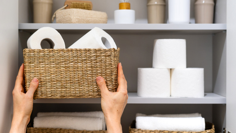 Person grabbing a basket with paper towel rolls in it